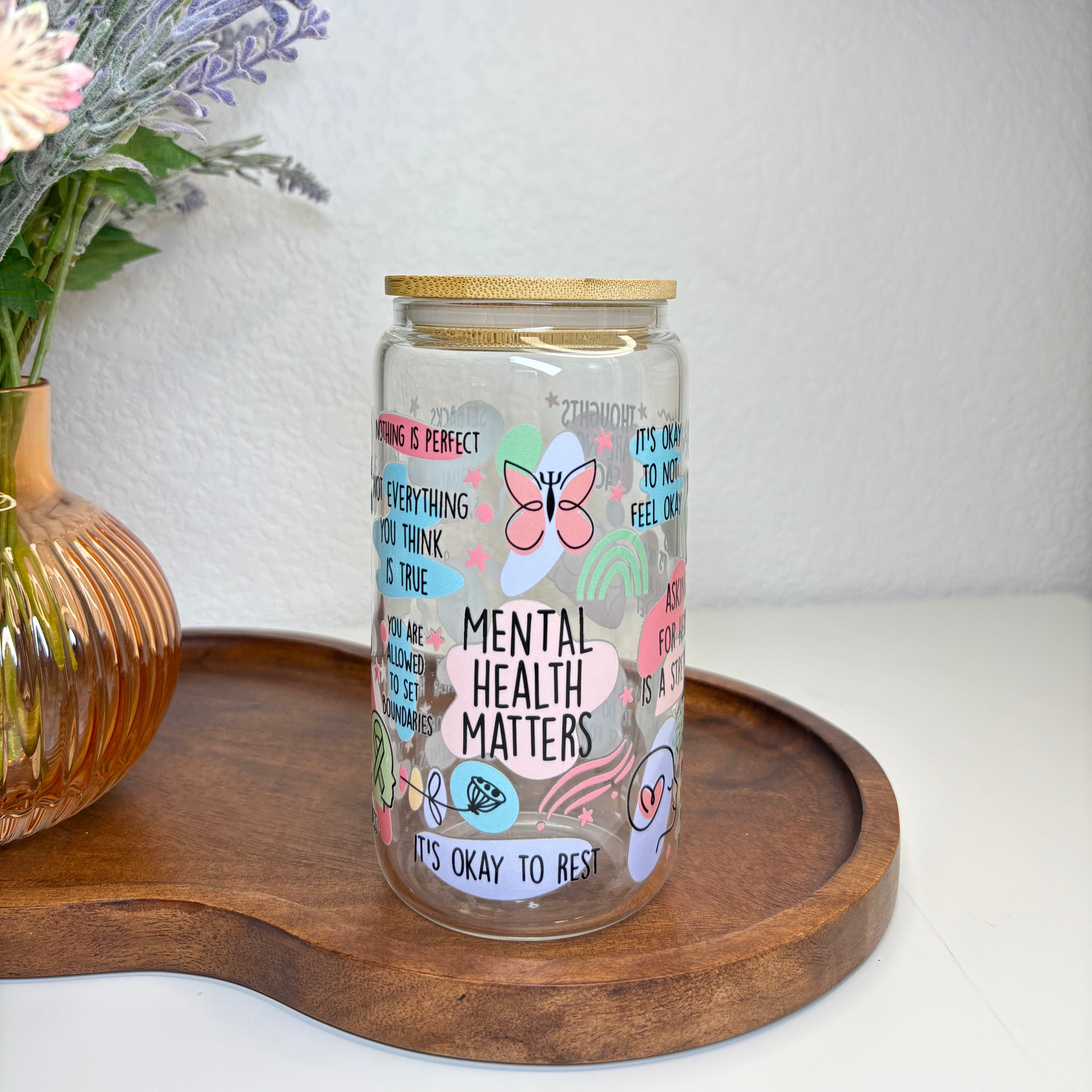 Glass jar with motivational text on a wooden tray with flowers in the background