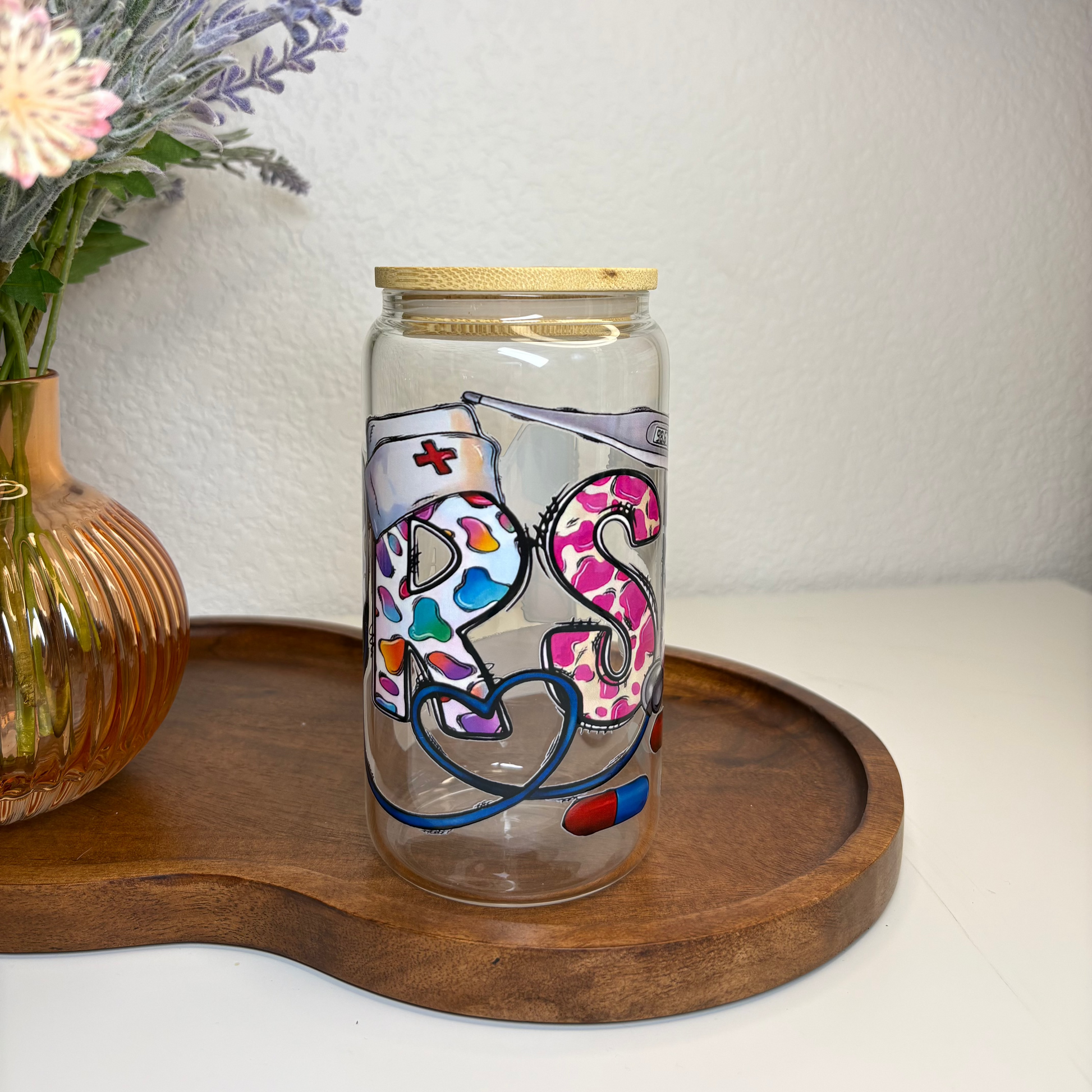 Decorative glass jar with colorful lettering on a wooden tray with flowers in the background